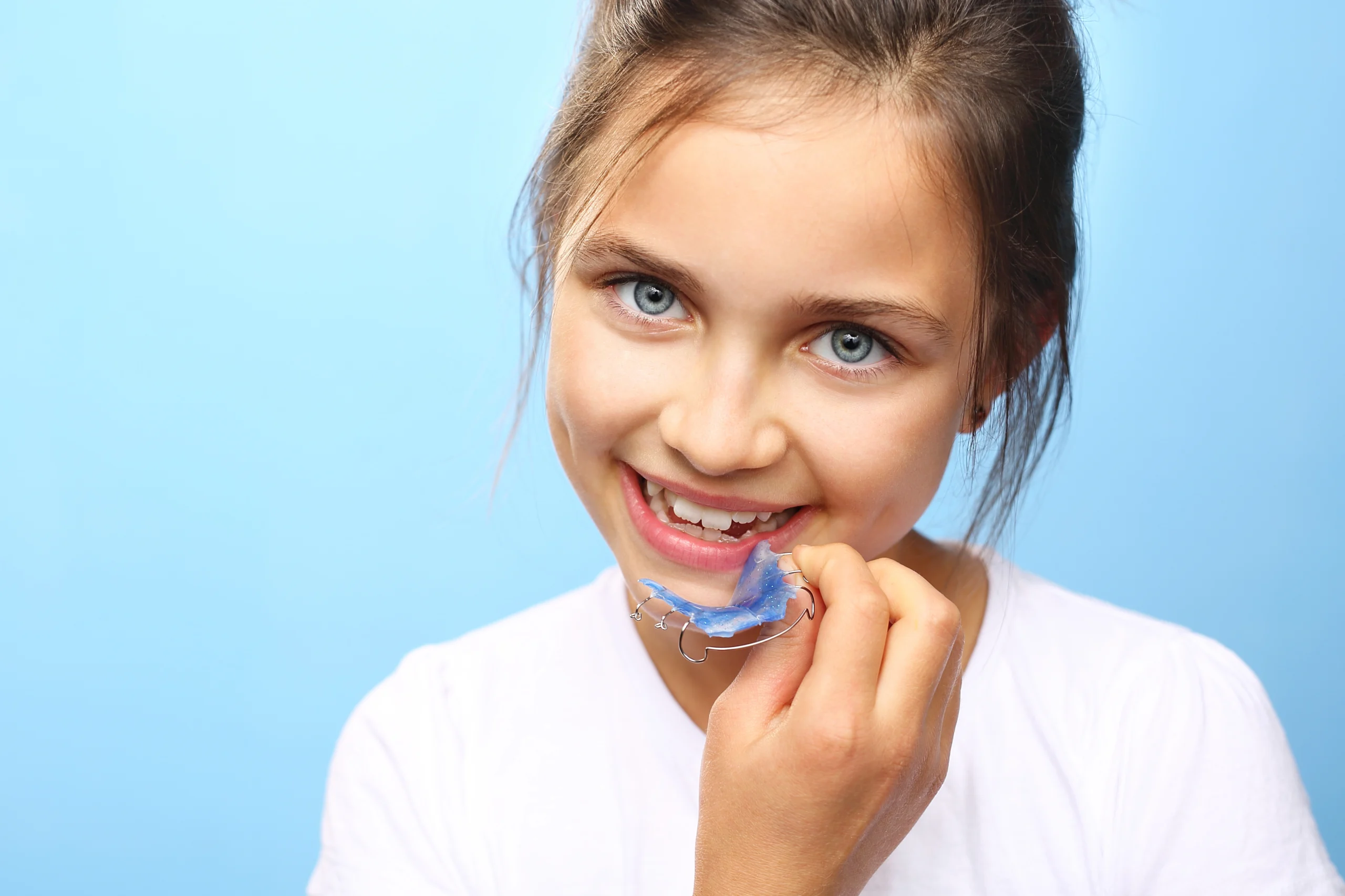 Mädchen mit blauen Augen lächelt und hält eine lose Zahnspange in der Hand – Kieferorthopädie für Kinder